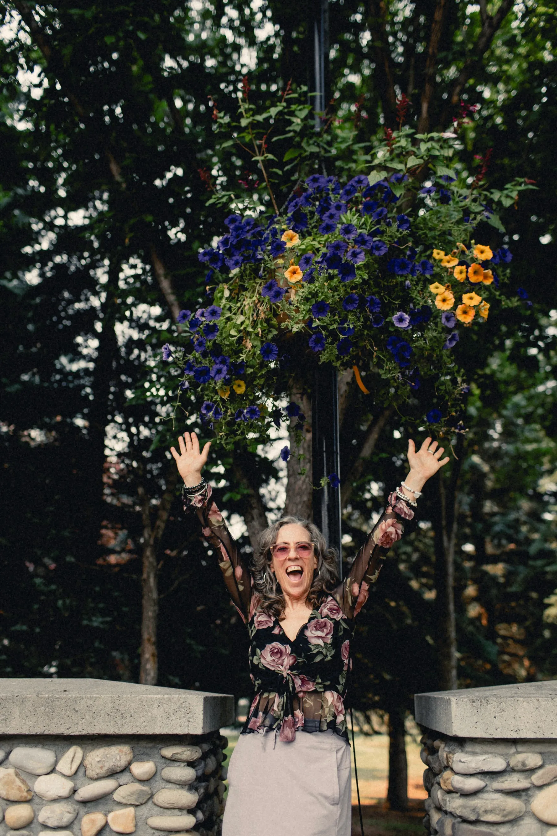 Heidi with her arms raised under hanging flowers