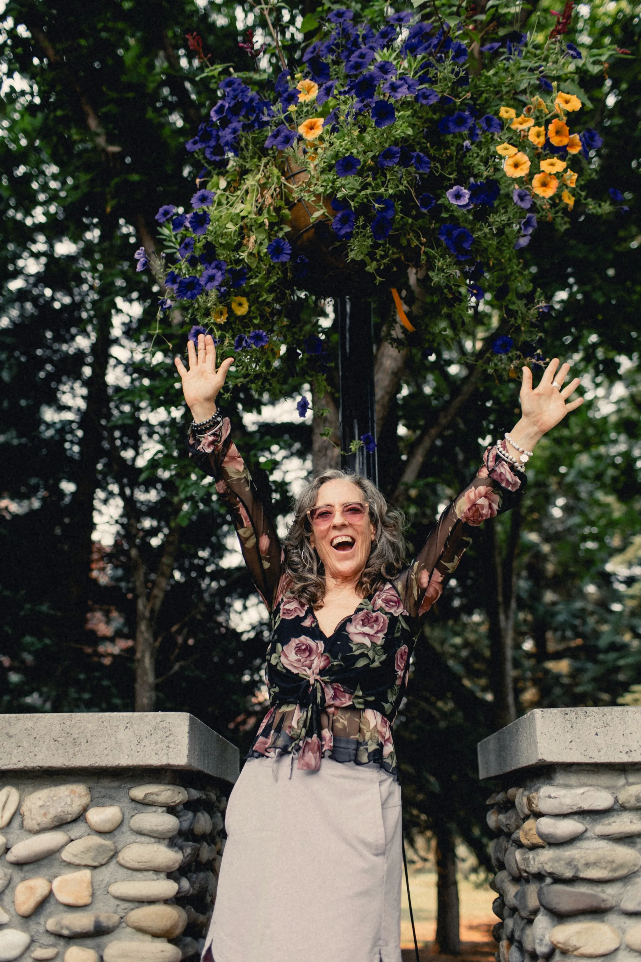 Heidi with her arms raised under hanging flowers