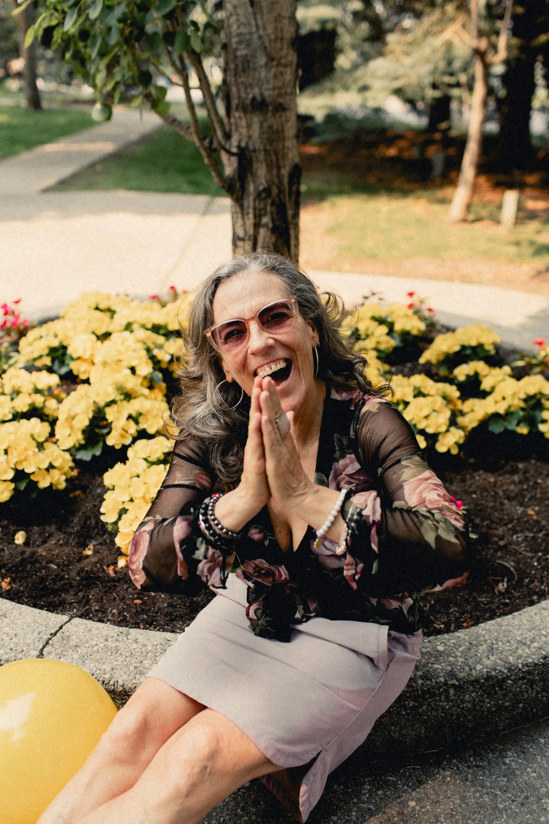 Heidi laughing beside a smiley-face ball in a flower bed