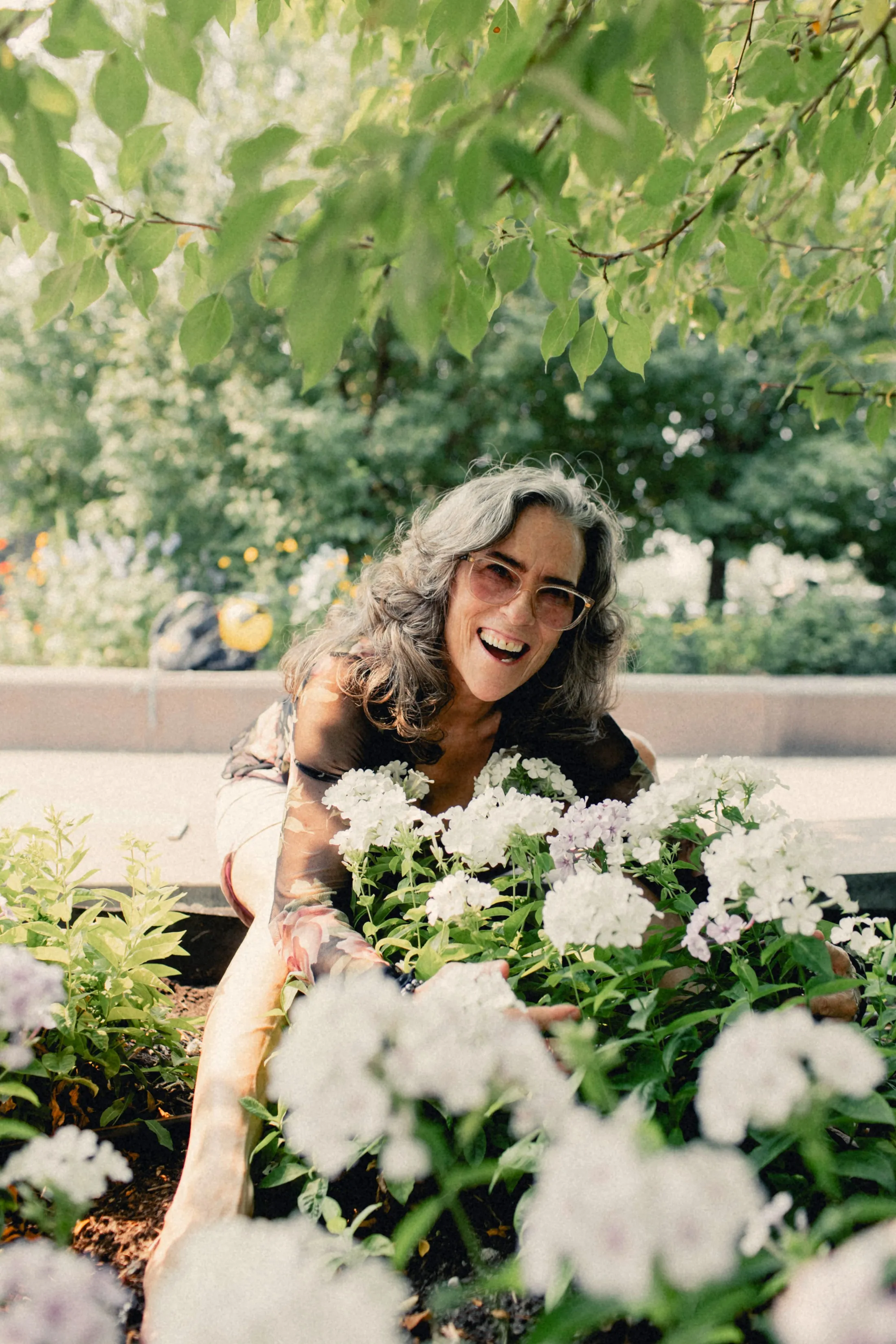 Heidi leaning into a bed of white flowers, laughing