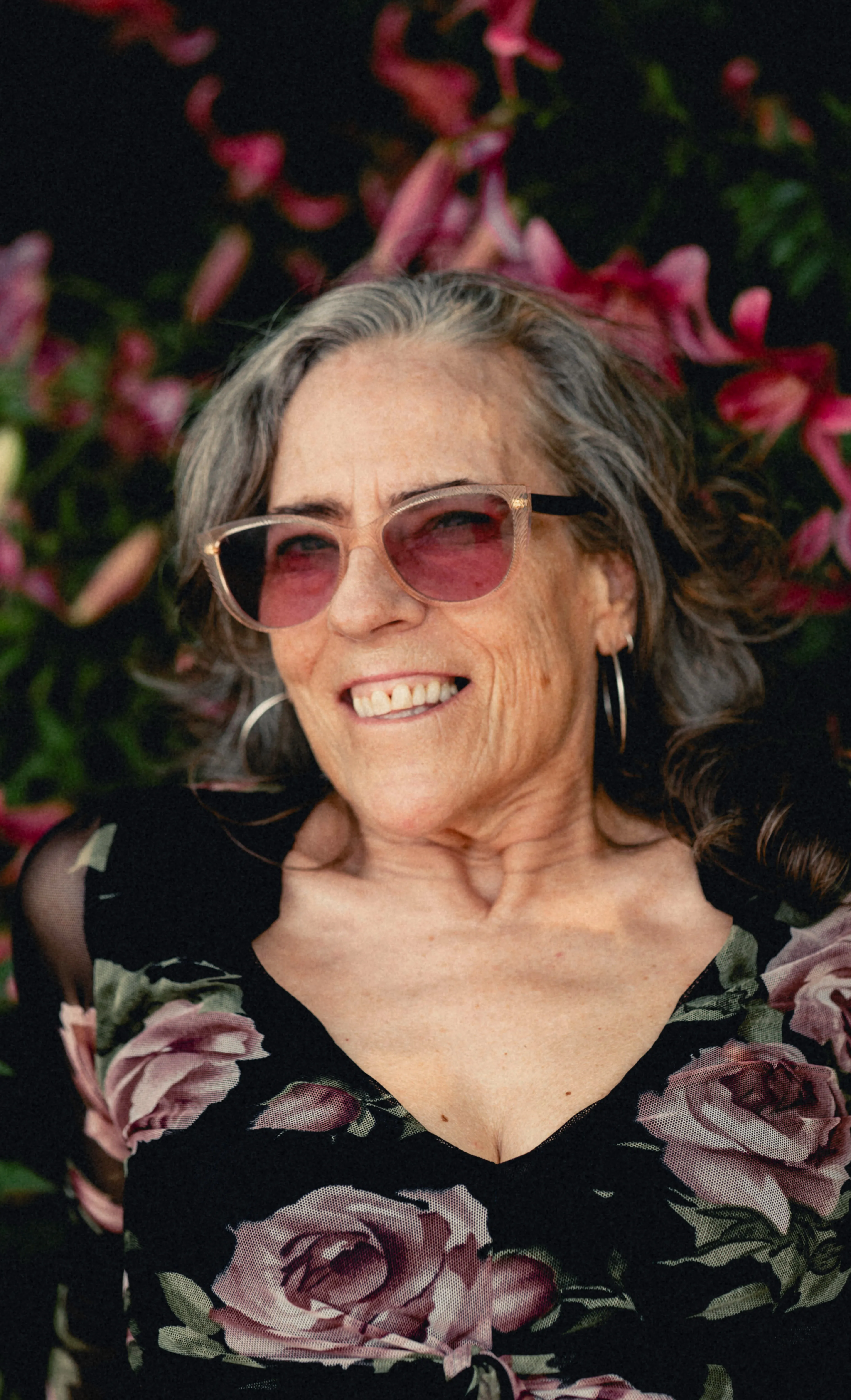 Heidi smiling in rose sunglasses among the flowers
