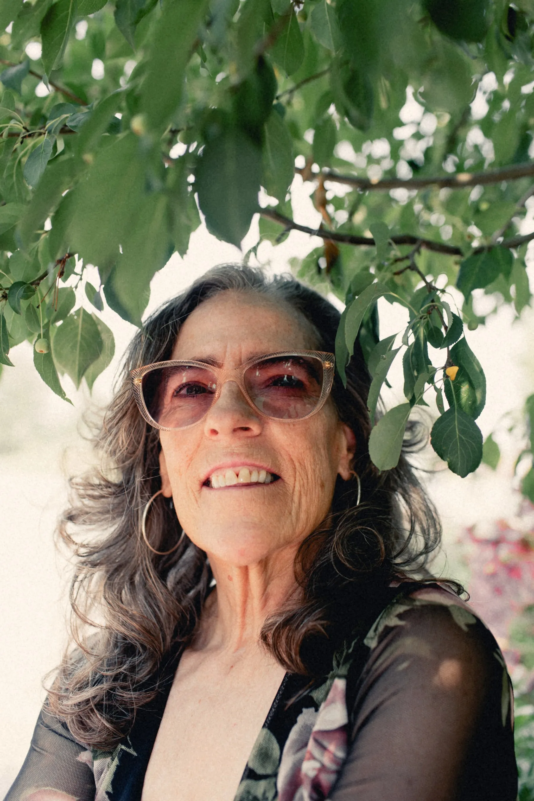 Heidi in pink sunglasses under green leaves