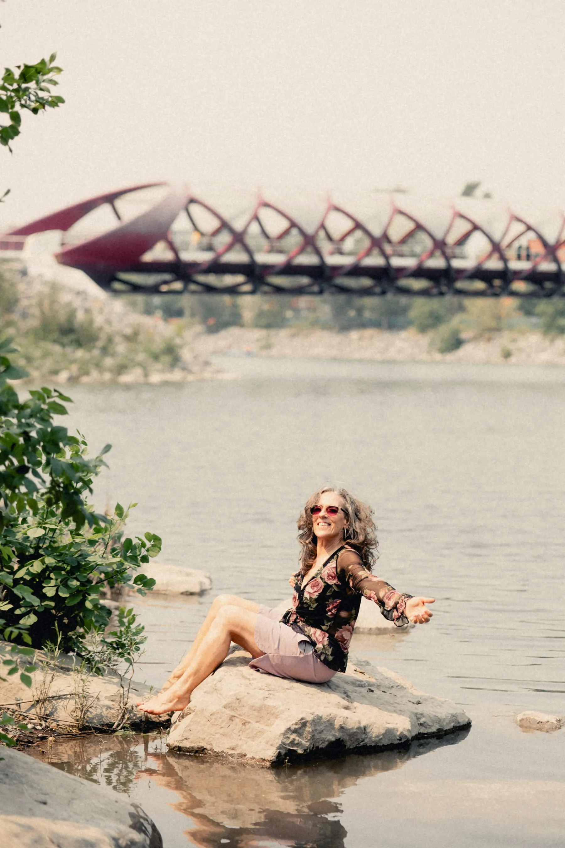 Heidi sitting on a rock in the river, Peace Bridge behind