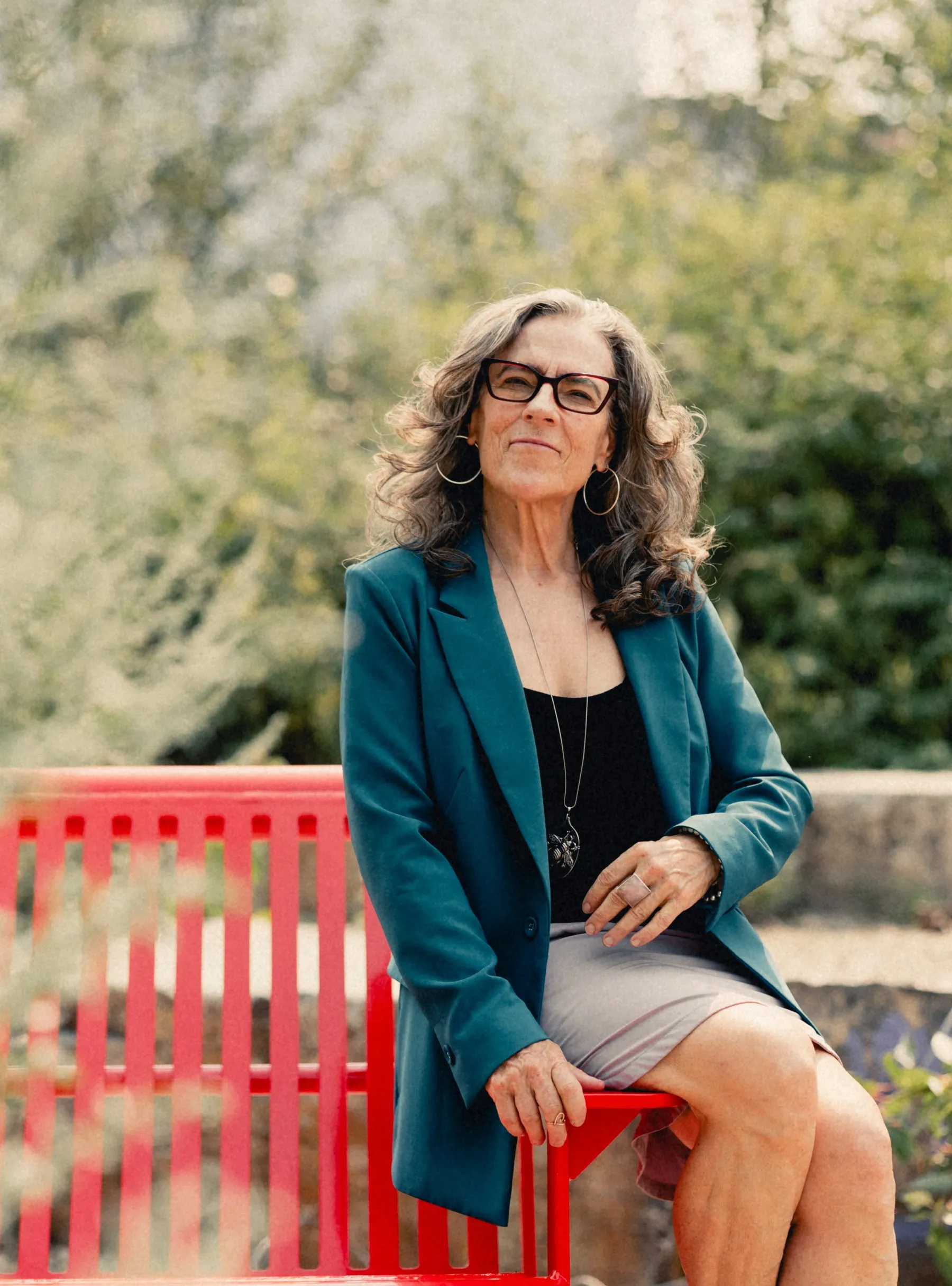 Heidi seated on a red bench in her teal blazer