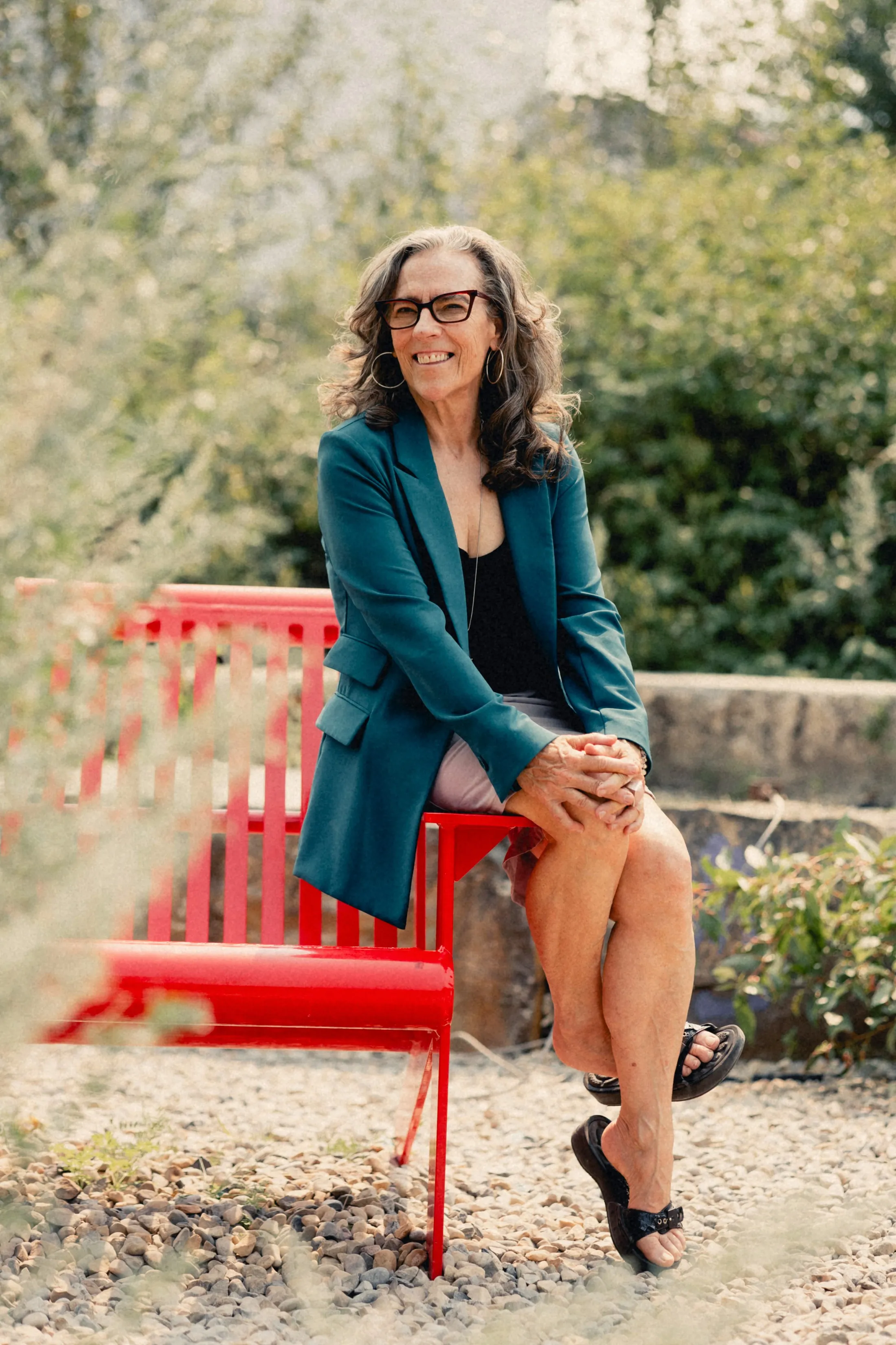 Heidi seated on a red bench, smiling, in her teal blazer