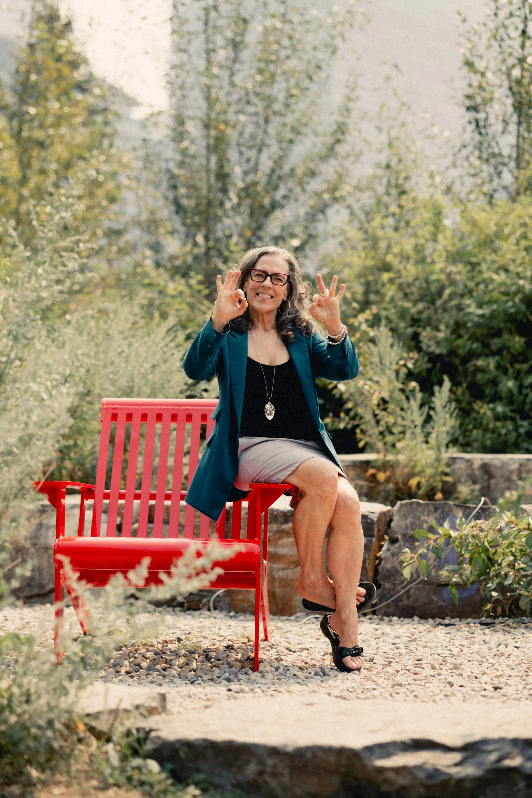 Heidi waving with both hands from a red bench