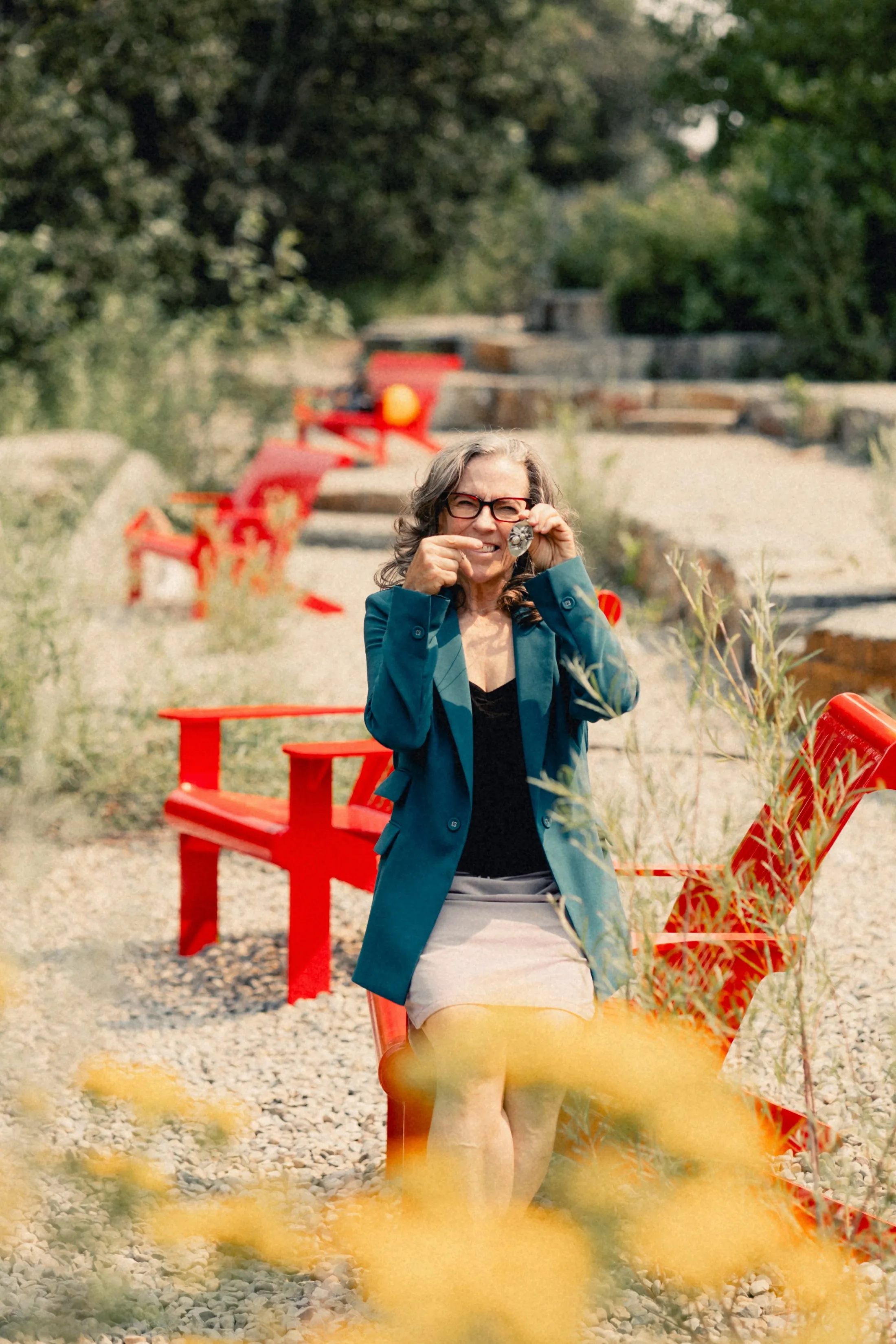 Heidi laughing on a red bench behind yellow flowers